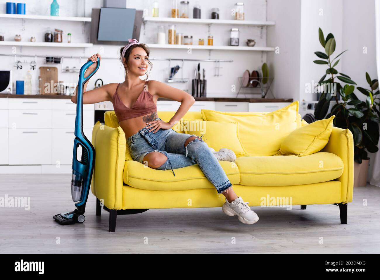 Femme au foyer avec la main sur la hanche regardant loin et tenant le vide nettoyant Banque D'Images