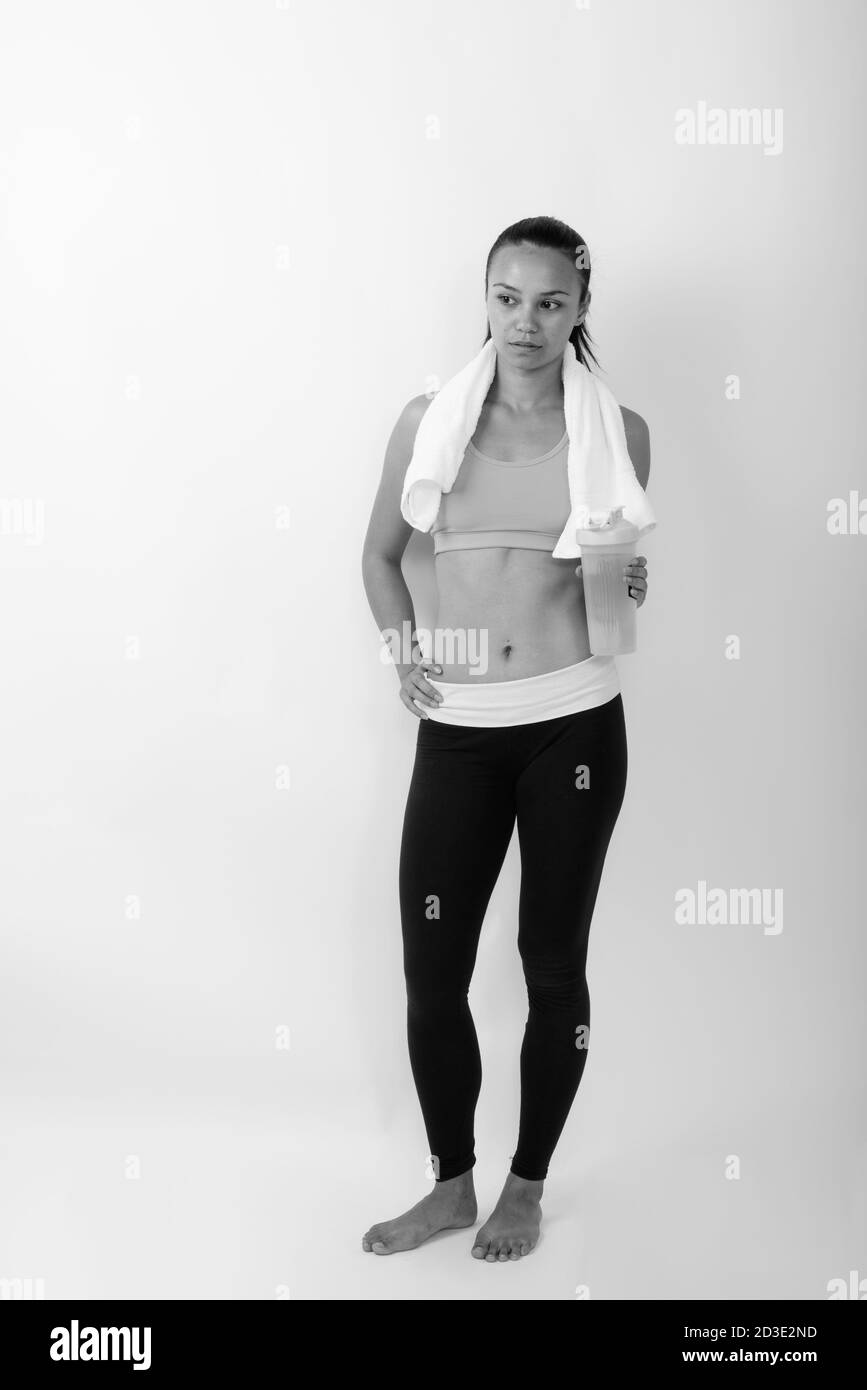 Photo de la jeune femme asiatique qui pense tout en tenant bouteille d'eau prête pour la salle de sport Banque D'Images