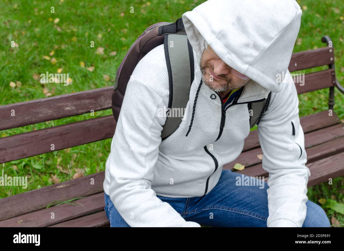Un homme d'âge moyen dans un pull à capuche assis seul un banc de parc Banque D'Images