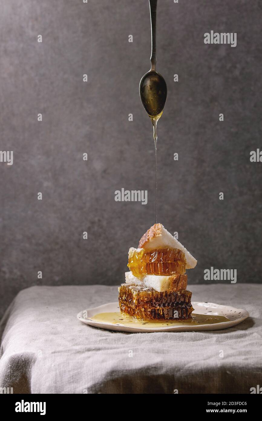 Miel d'abeilles et du miel qui coule dans de cuillère pour tranches de pain de blé chez le plaque en céramique sur le linge de table cloth avec mur gris à l'arrière Banque D'Images