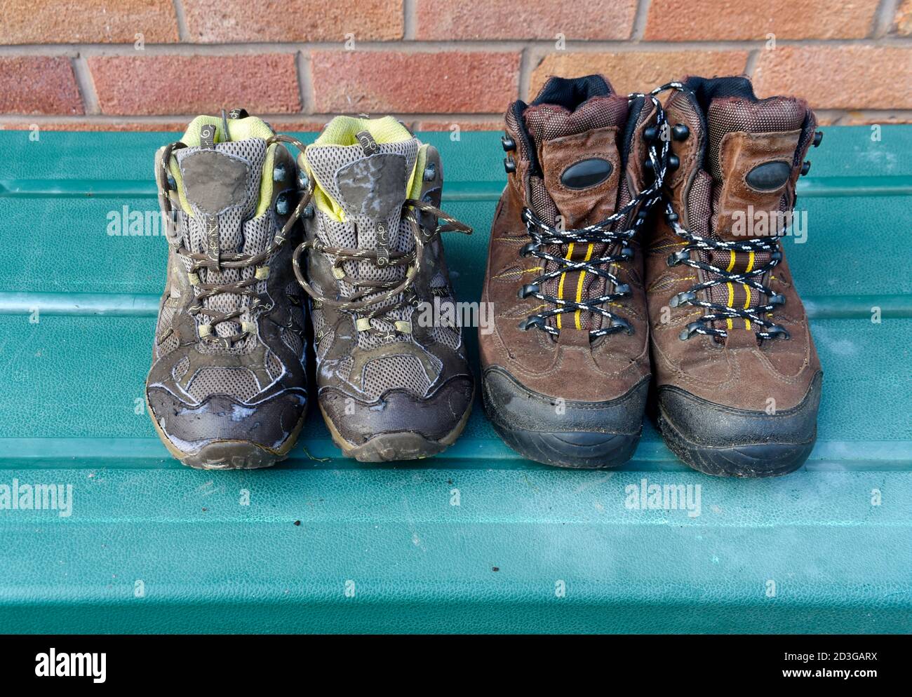 gros plan de 2 paires de chaussures de marche brunes à l'extérieur, séchage au soleil, bottes sales pour hommes et femmes sur boîte verte avec mur en brique en arrière-plan Banque D'Images
