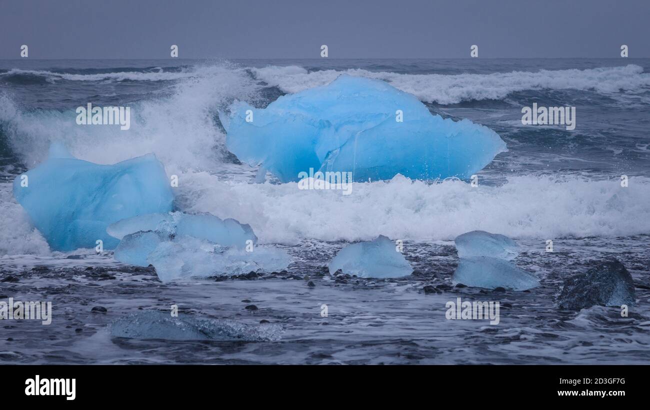 Les vagues de marée repoussent les morceaux de glace glaciaires sur la plage noire près de Jokulsarlon, dans le sud-est de l'Islande Banque D'Images