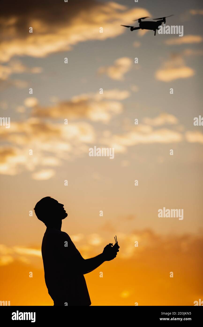 Silhouette d'un jeune homme utilisant un drone dans UN Cadre rural au coucher du soleil Banque D'Images