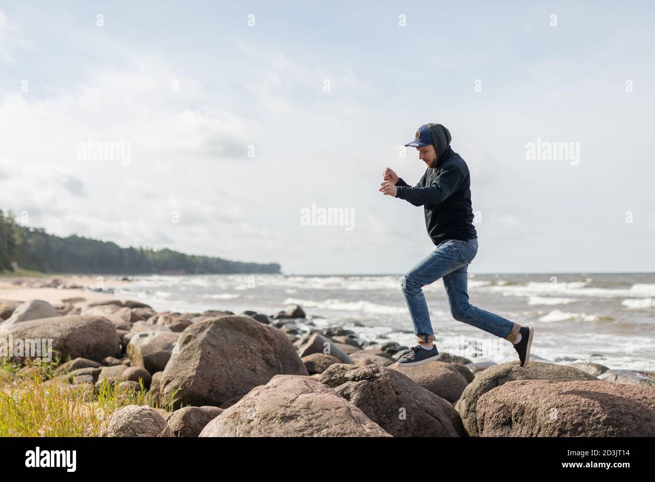 Un jeune homme s'amusant sur la plage de Baltic See, passant d'un grand rocher à l'autre Banque D'Images