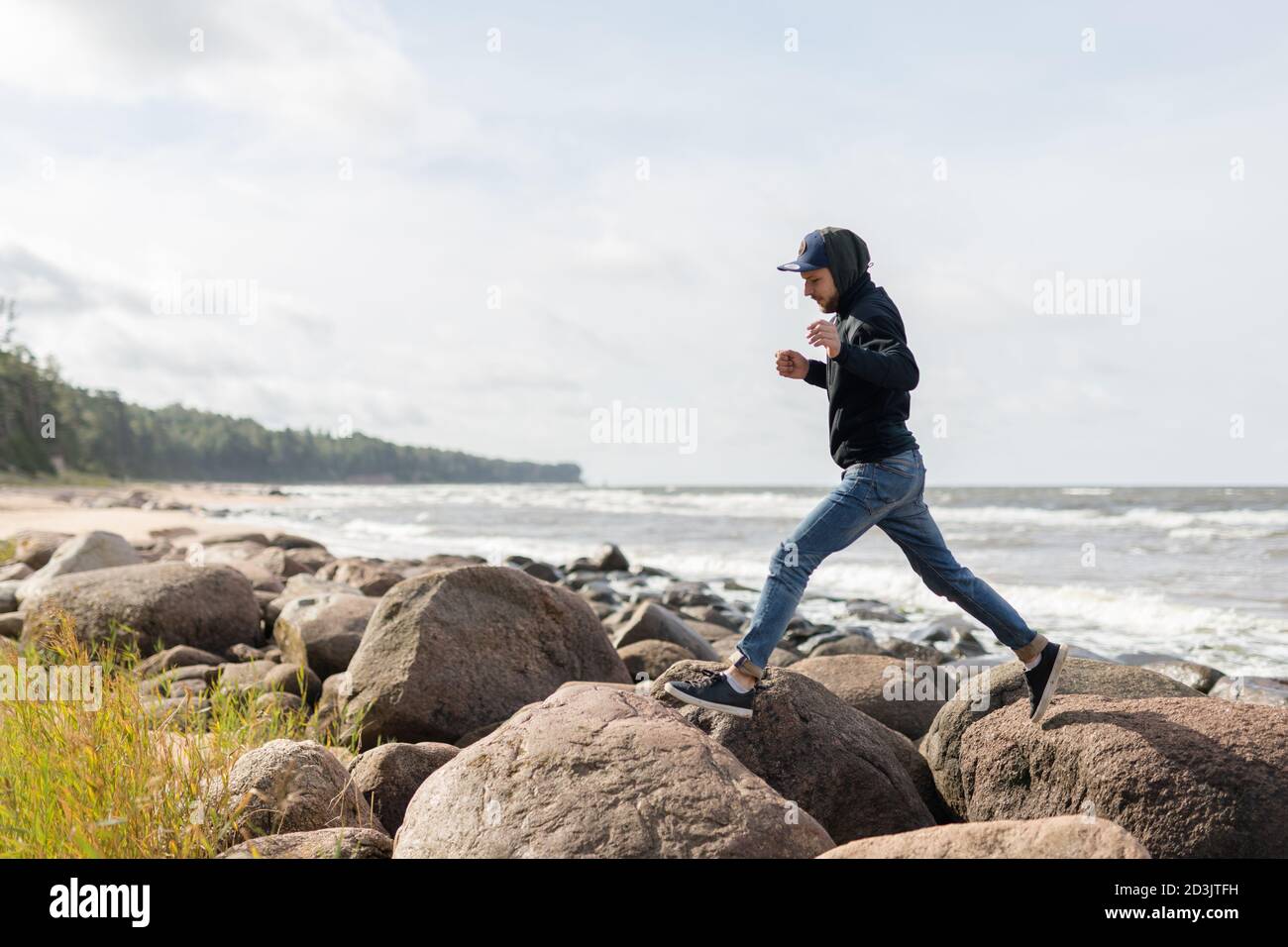 Un jeune homme s'amusant sur la plage de Baltic See, passant d'un grand rocher à l'autre Banque D'Images