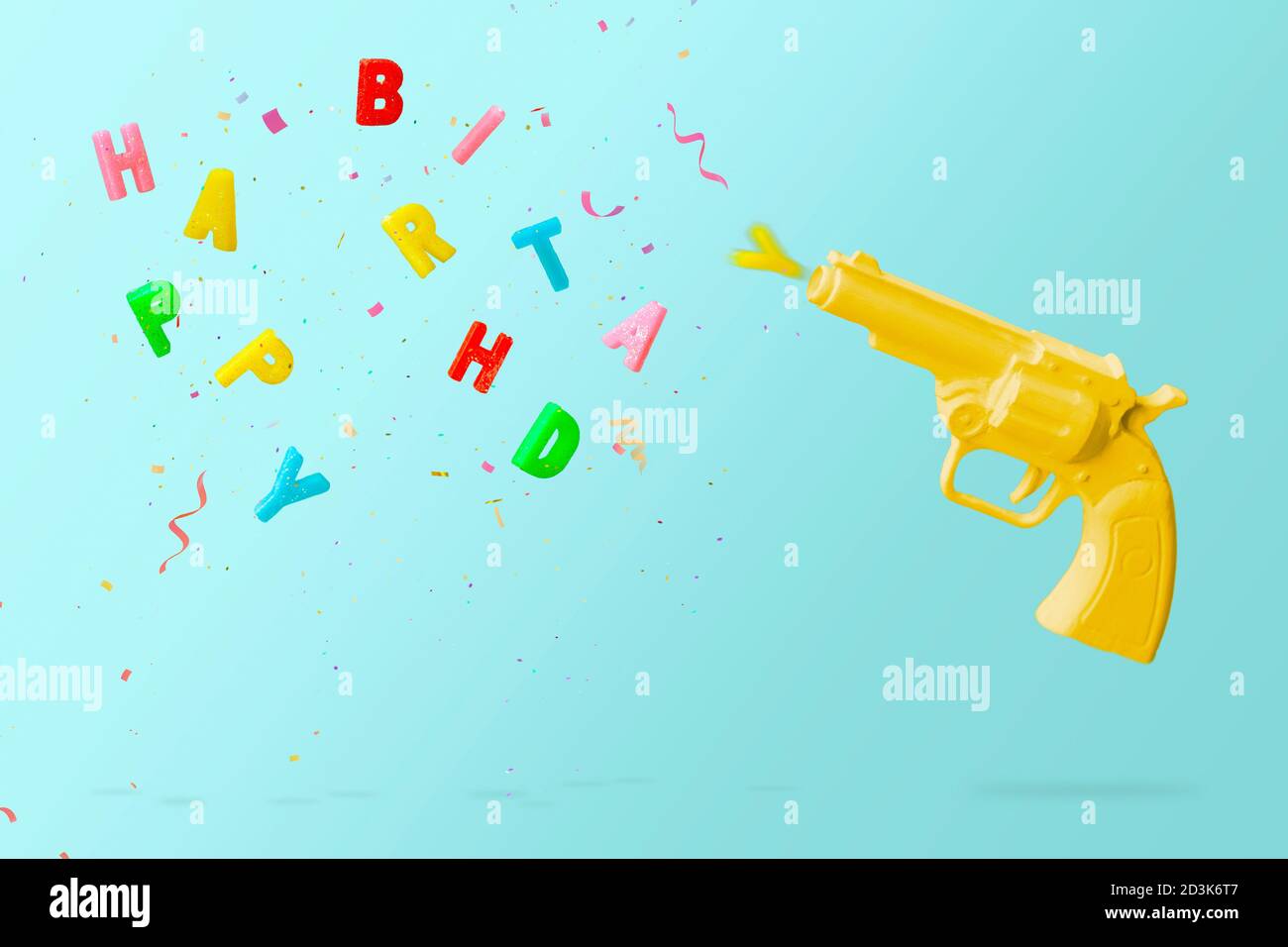 Pistolet jaune tir bougies d'anniversaire colorées et confetti colorés, sur fond bleu. Concept joyeux anniversaire avec espace copie Banque D'Images