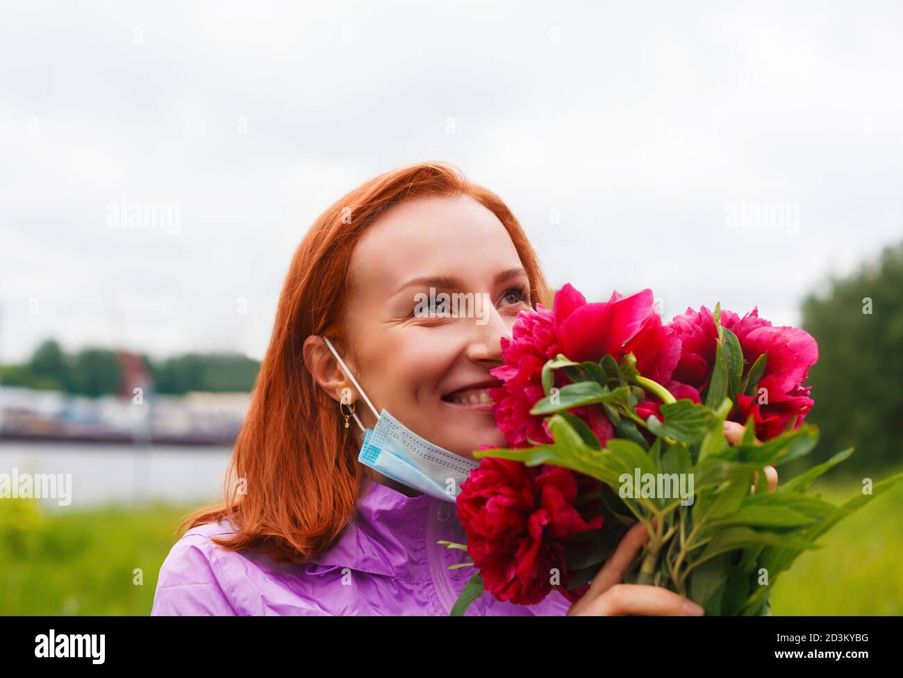 Reprise après le coronavirus. Souriante heureuse femme rouge sniffs fleurs roses Banque D'Images