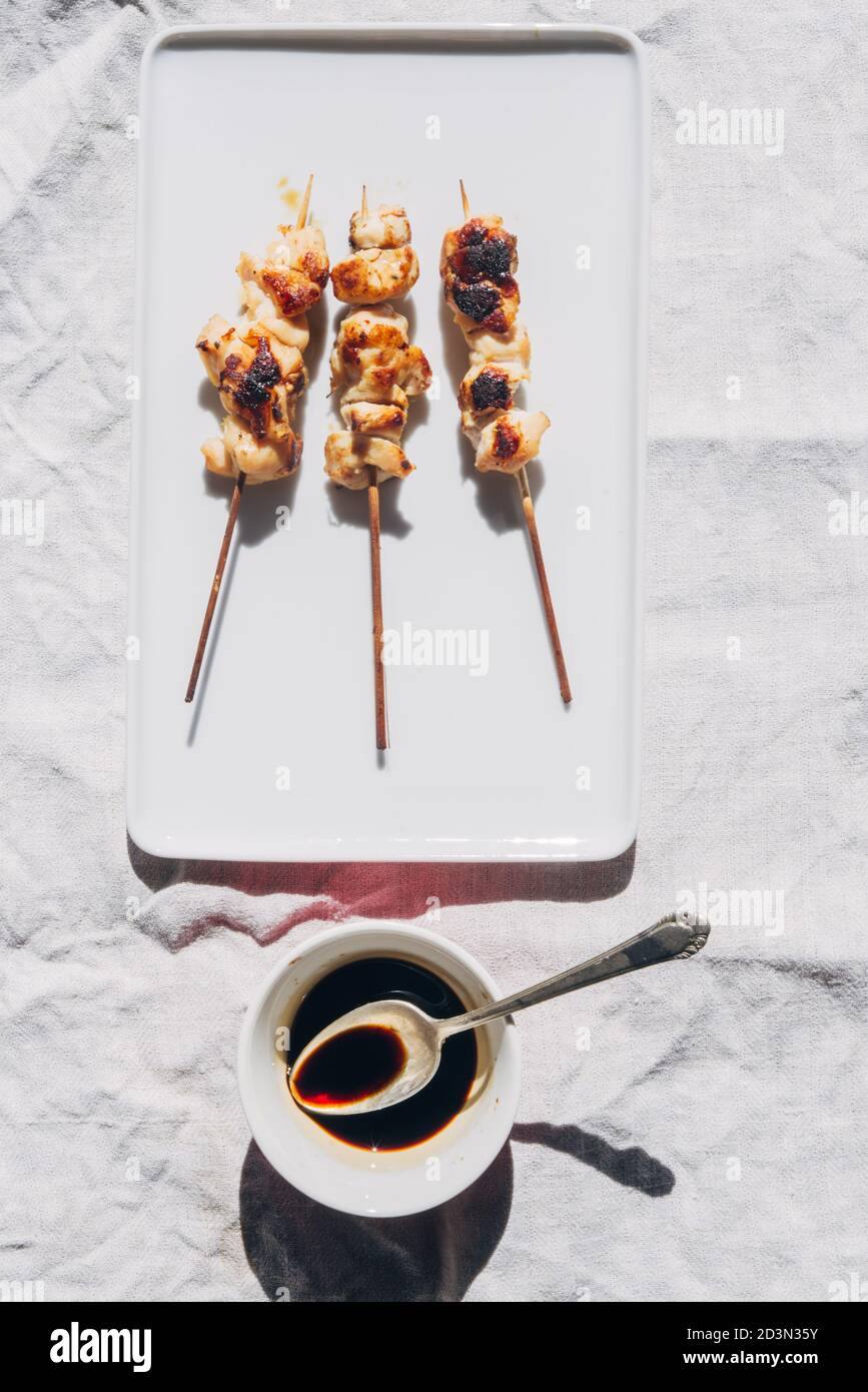 Petites pièces brochette de poulet sur un plat blanc avec sauce soja sur un petit récipient, sur une table en bois rustique bleu, thème barbecue, lumière dure avec defi Banque D'Images