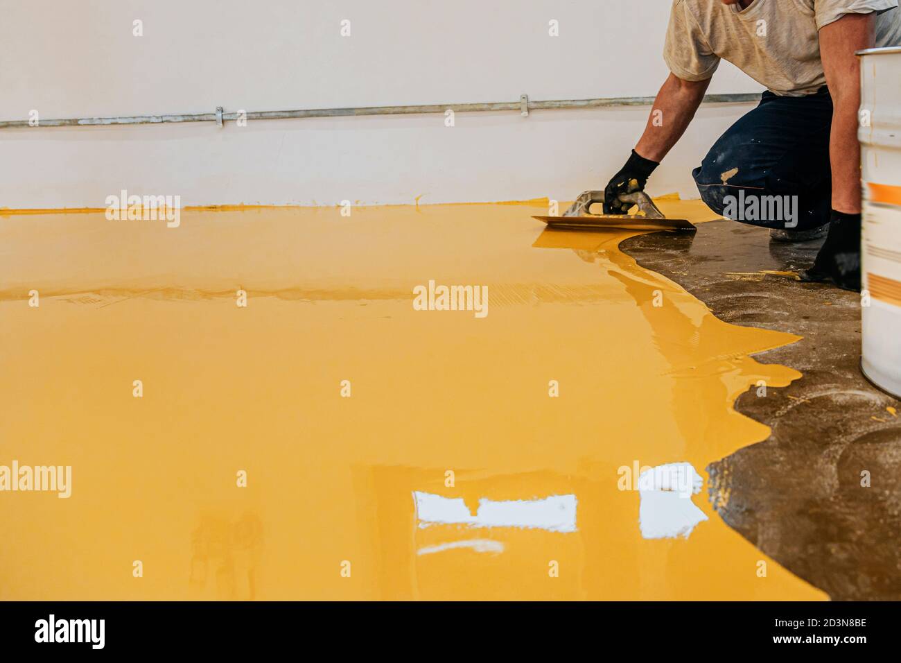 Ouvrier, revêtement de sol avec de la résine époxy auto-nivelante dans un atelier industriel. Banque D'Images