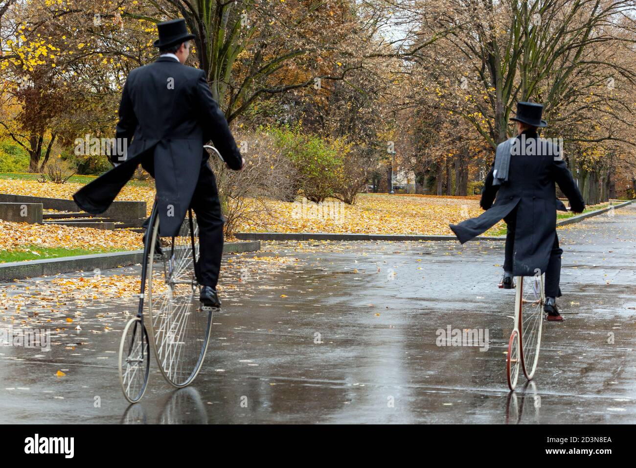 Deux cyclistes traversent le parc d'automne de Penny Farthing bicyclettes portant un revêtement de queue Banque D'Images