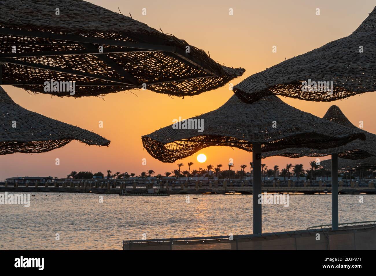 Lever de soleil sur la plage avec des parasols et des palmiers à Hurghada, en Égypte. Banque D'Images