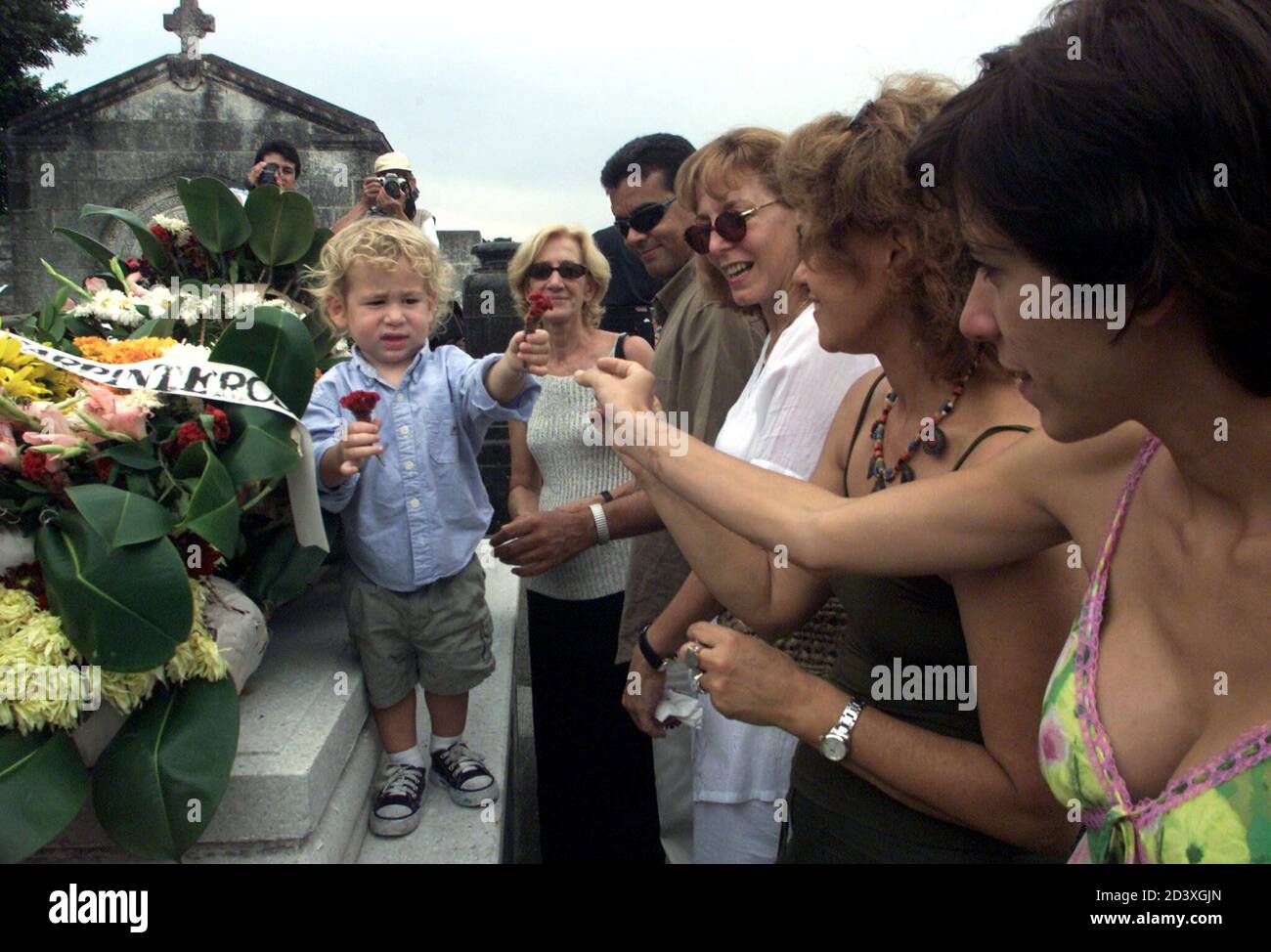 Anan Rodes (L), petit-fils du photographe cubain Alberto Korda, remet des  fleurs à des parents lors des funérailles de son grand-père le 29 mai 2001  dans la cimenterie Colon de la Havane.