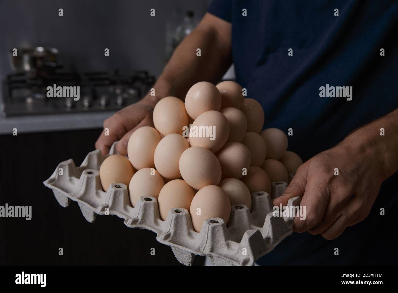 un homme tenant un plateau plein d'oeufs de poulet dedans sa propre cuisine Banque D'Images