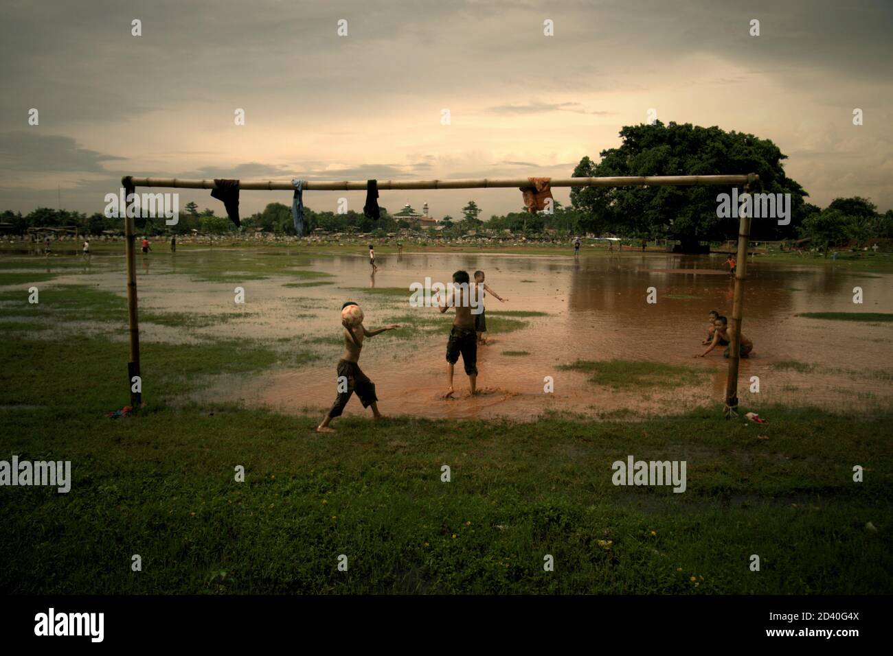 Les enfants jouent au football sur un terrain partiellement inondé, situé entre deux cimetières publics à Pondok Kelapa, Jakarta, Indonésie. Banque D'Images