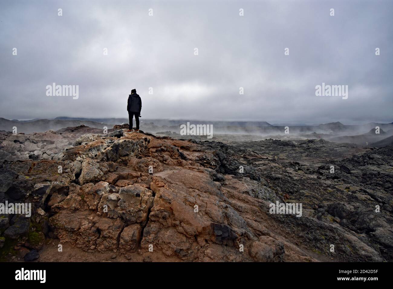 Un homme portant des stands noirs dans les champs de Krafla Lava dans la région du lac Myvatn dans le nord de l'Islande.Steam s'élève de la roche volcanique un jour couvert. Banque D'Images