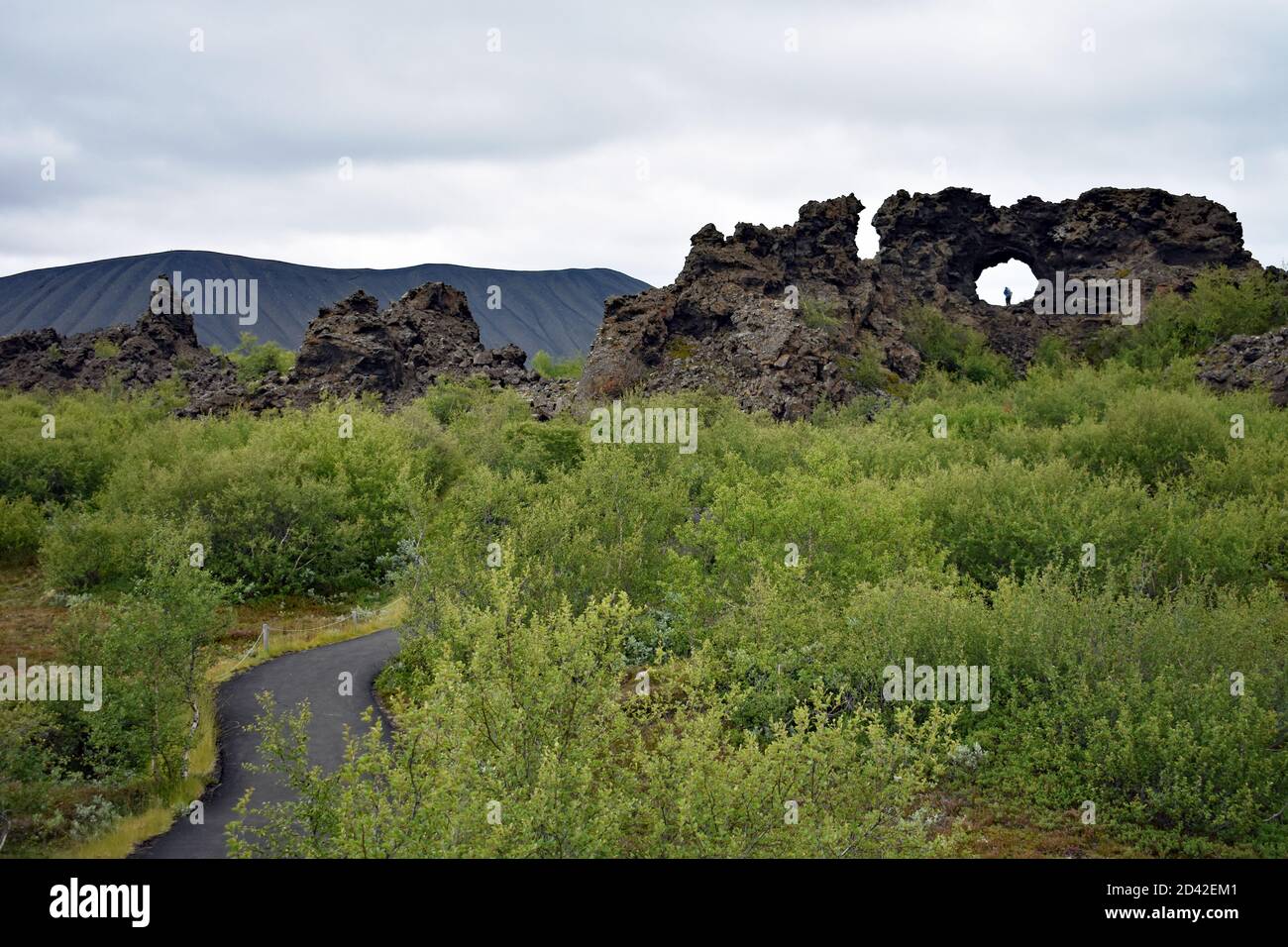 Le champ de lave à Dimmuborgir dans le lac Myvatn, au nord de l'Islande. Un chemin piétonnier à travers les arbres. Une fenêtre en lave avec un visiteur à l'intérieur. Hvertomba derrière. Banque D'Images