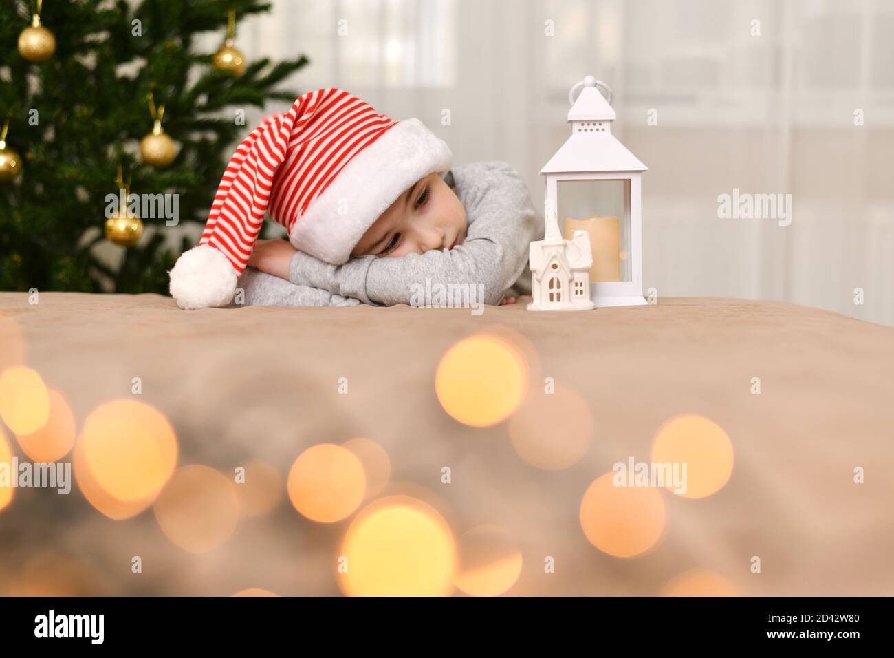 Un enfant triste dans une casquette rayée se trouve à l'arbre de Noël. Banque D'Images
