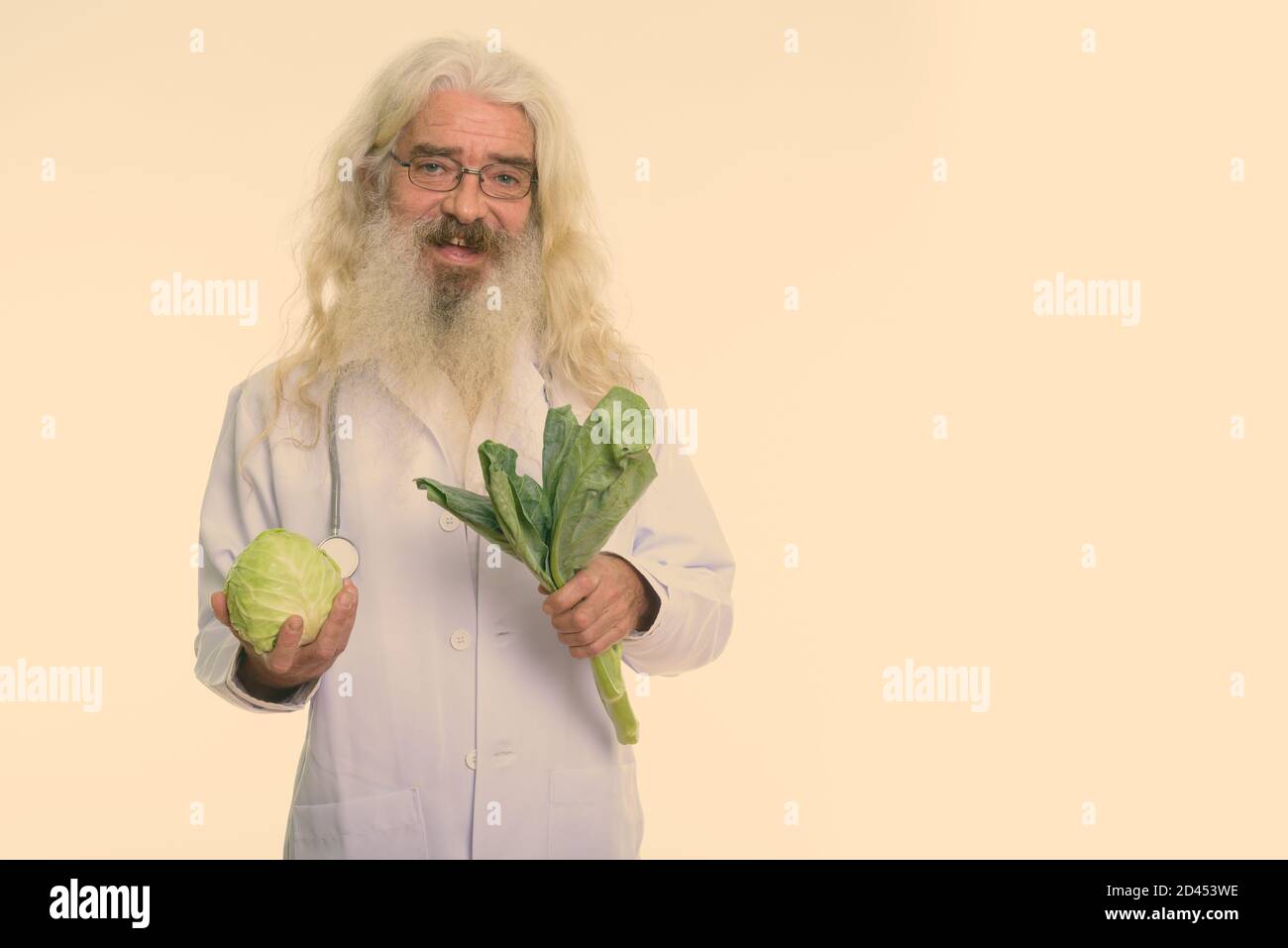 Studio shot of happy senior homme barbu doctor smiling en maintenant le chou et les légumes Banque D'Images