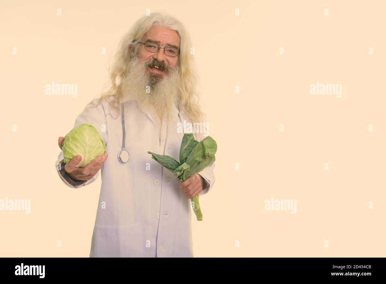 Studio shot of happy senior man smiling médecin barbu tout en donnant le chou et holding vegetables Banque D'Images