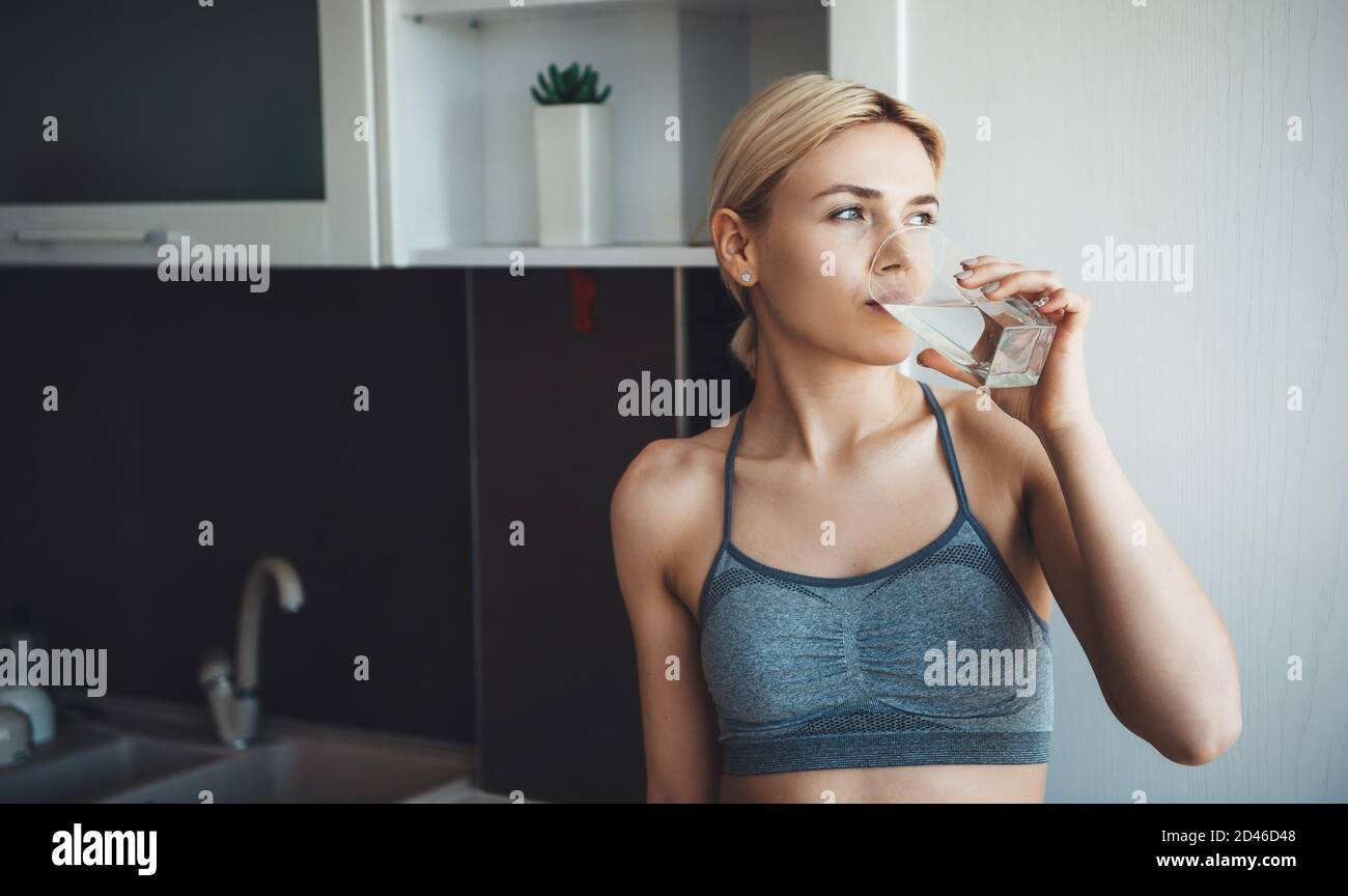 Charmante femme caucasienne avec des cheveux blonds portant des vêtements de sport est de boire un verre d'eau pendant les cours de fitness numérique à accueil Banque D'Images
