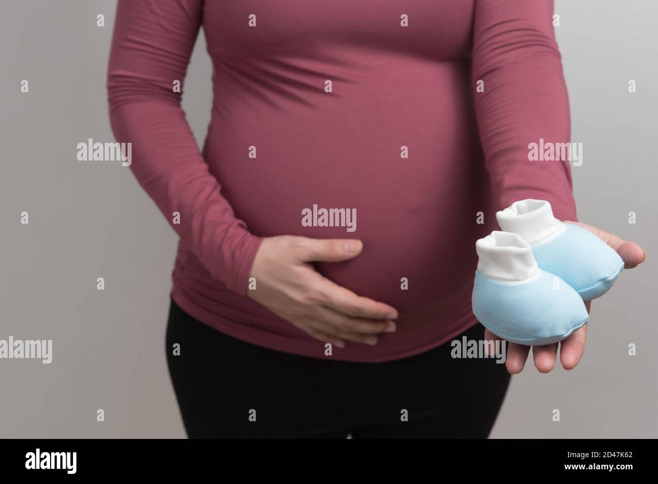 Gros plan sur le corps de la femme enceinte asiatique avec t-shirt à  manches longues rouge tenant la jolie chaussure bleue pour bébé, portrait  léger studio et espace de copie sur le