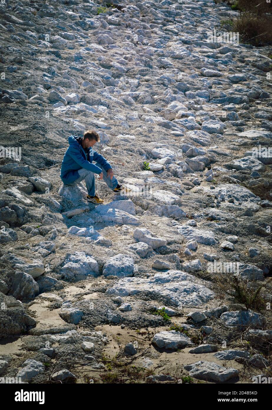 Homme découragé assis dans un paysage rocheux stérile. Banque D'Images