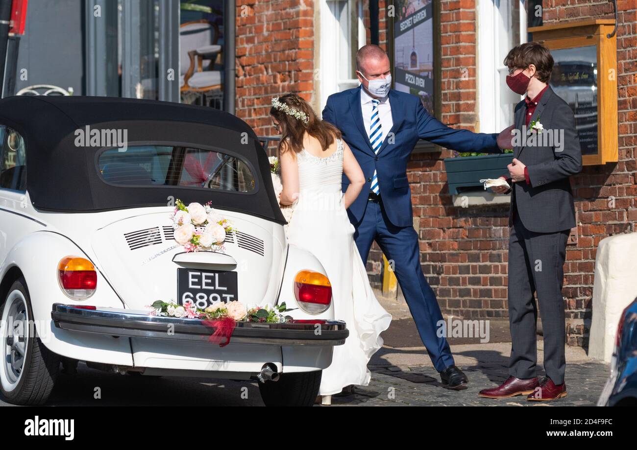 Un couple portant un masque de visage entrant dans une voiture de mariage lors d'un événement COVID SAFE lors de la pandémie du coronavirus COVID19 à West Sussex, en Angleterre, au Royaume-Uni. Banque D'Images