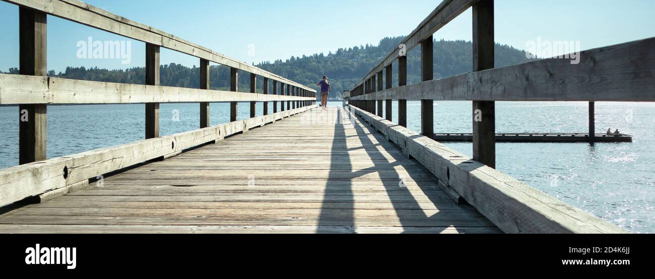 Femme marchant sur un pont en bois ou un quai d'expédition. Ciel bleu et eau. Concept de loisirs. Banque D'Images