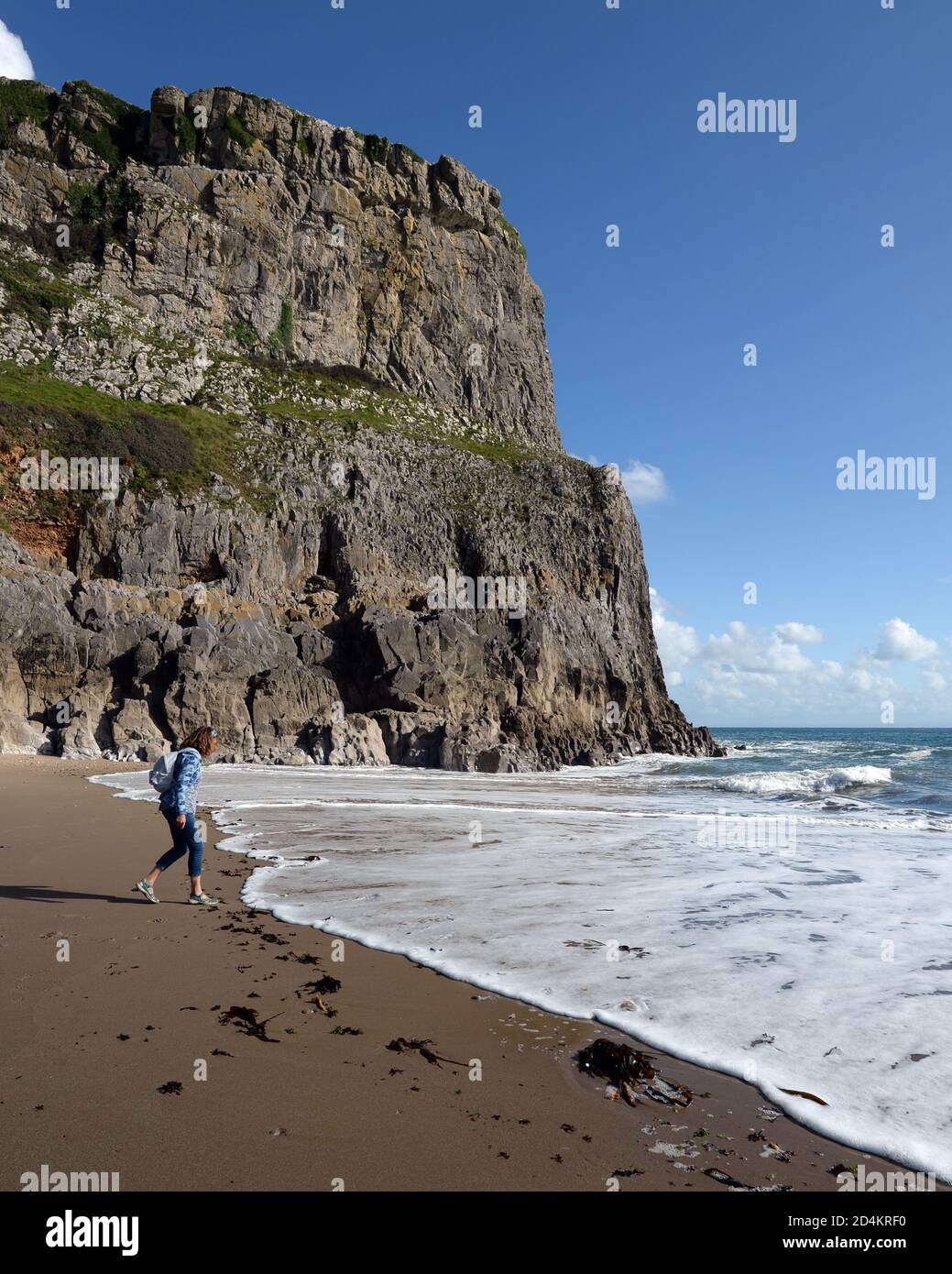 Une femme court pour éviter les vagues à Fall Bay -une plage de sable abritée à marée basse entourée d'une pente raide falaises de calcaire et paysages magnifiques Banque D'Images