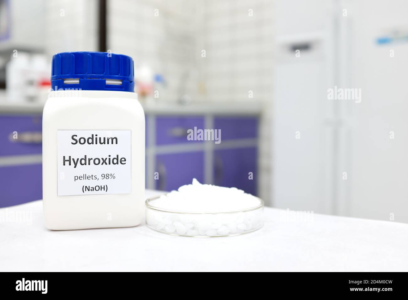 Mise au point sélective d'une bouteille d'hydroxyde de sodium pur ou de composé chimique NaOH à côté d'une boîte de Petri avec des pastilles solides blanches. Laboratoire de recherche en chimie. Banque D'Images