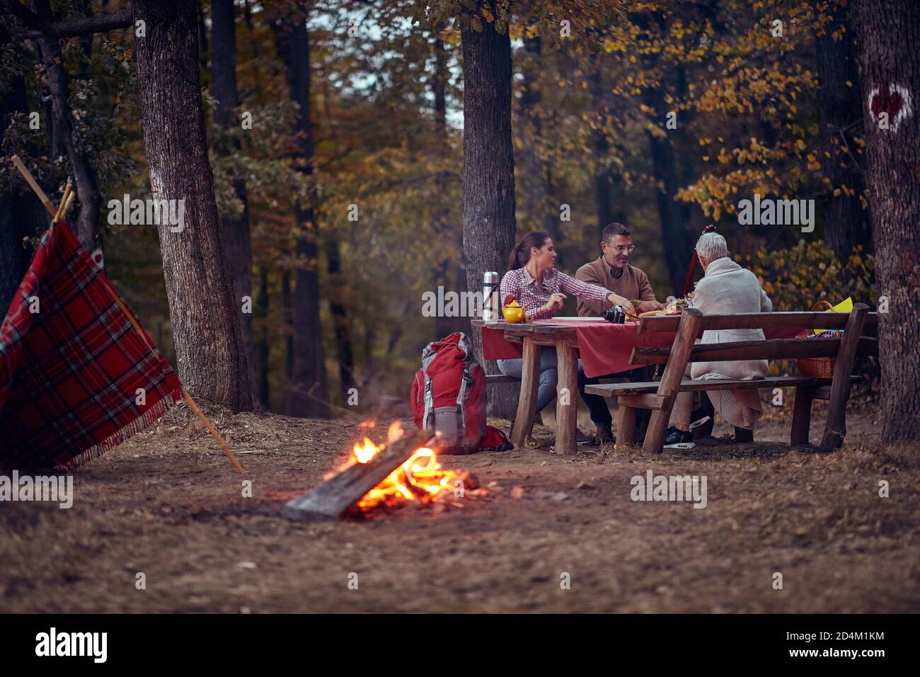 Un couple de personnes âgées et leur fille qui pique-nique la forêt autour d'un feu de camp sur un beau crépuscule d'automne Banque D'Images