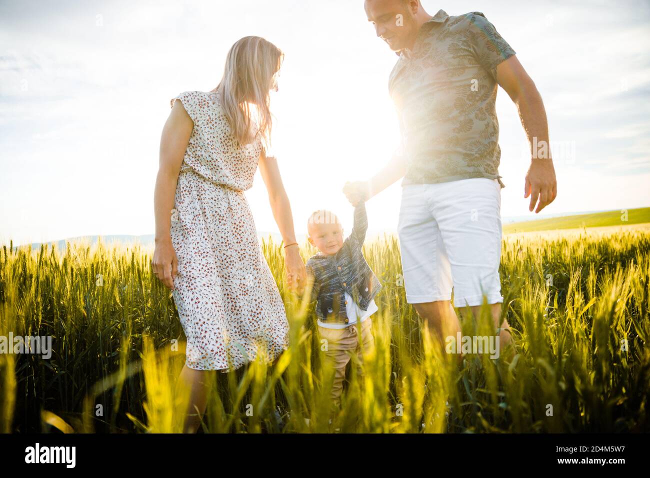Bonne famille dans l'herbe verte lumineuse au coucher du soleil. Banque D'Images