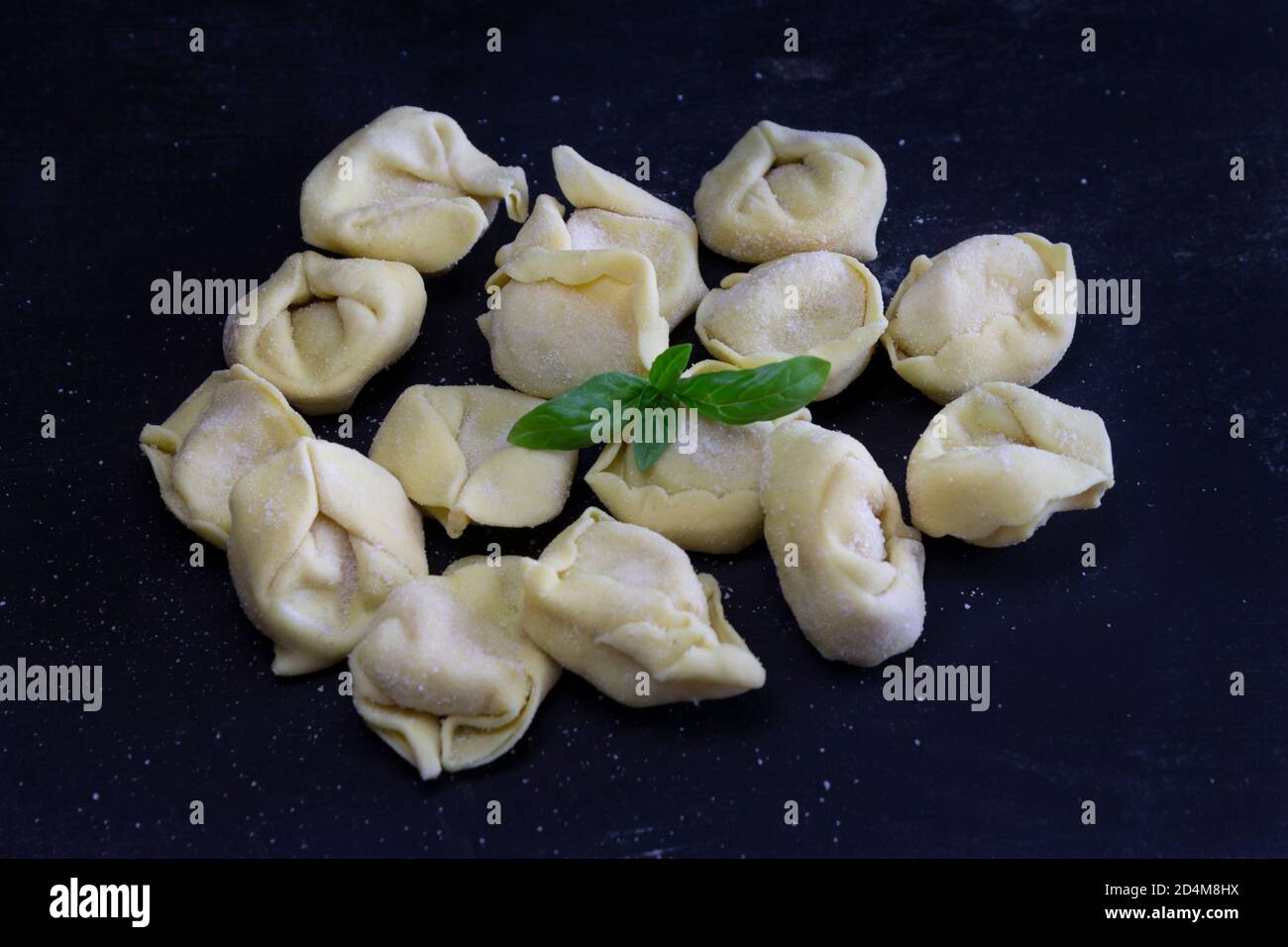 Raviolis au basilic sur fond noir et fleuri. Cuisine italienne maison saine concept.processus de fabrication des raviolis au pesto italien. Banque D'Images