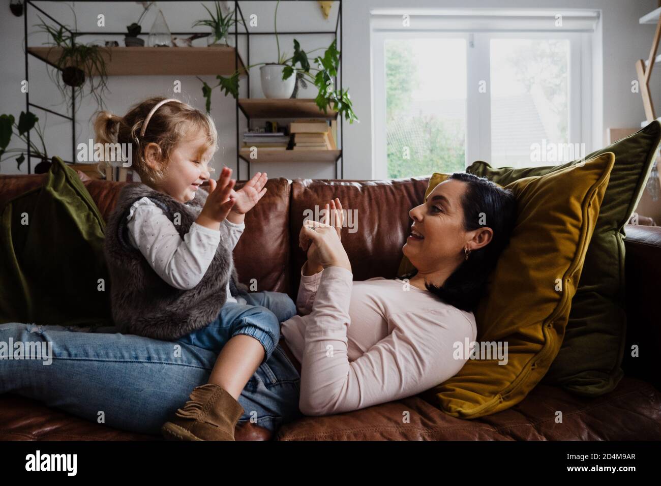 La mère et la petite fille caucasiennes jouent sur le canapé à la maison, chatouillant et riant Banque D'Images