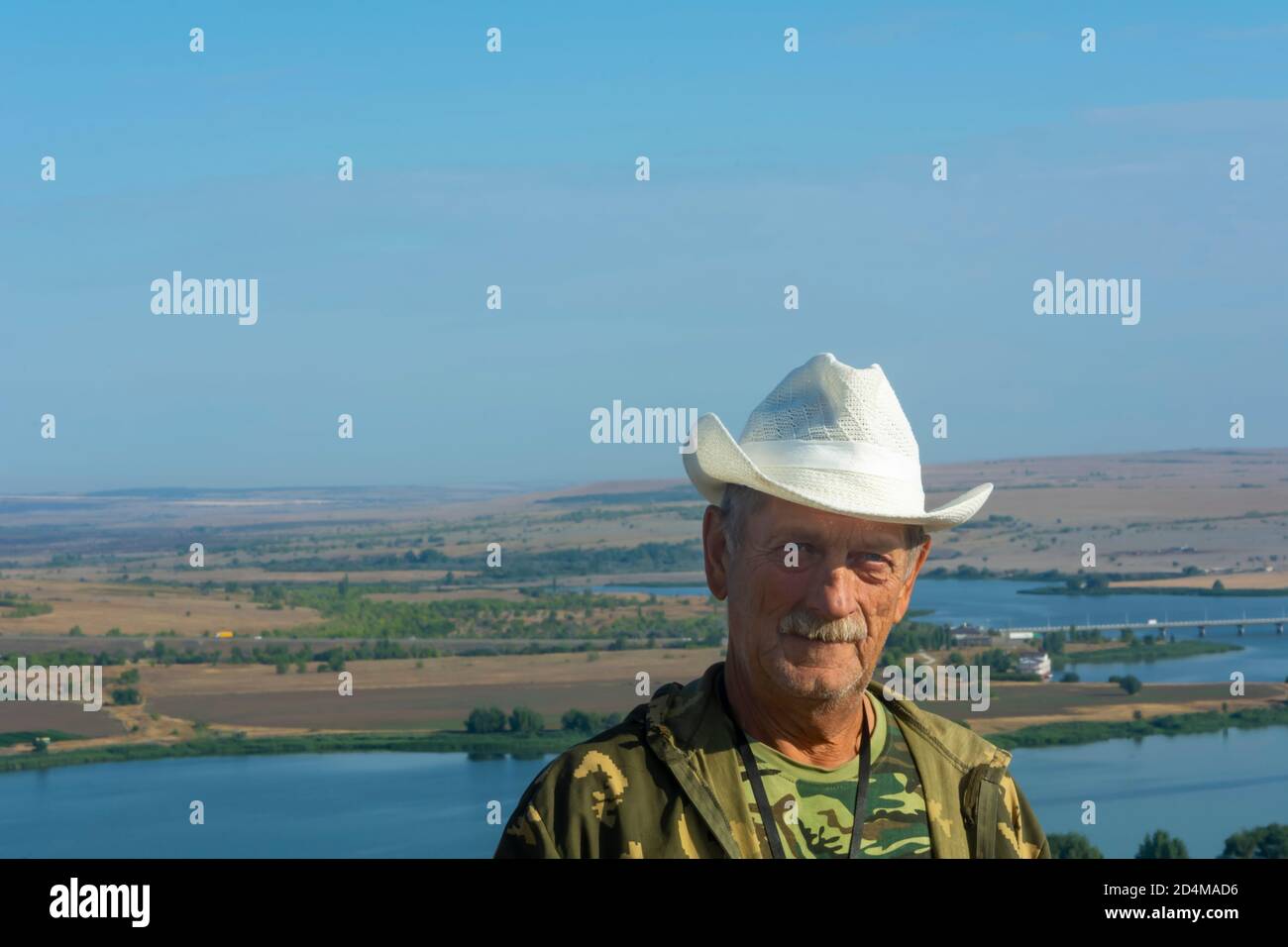 Un homme plus âgé en chapeau de paille blanc regarde la caméra sur fond de rivière et de nature. Concept de style de vie des aînés. Espace de copie, mise au point douce, flou. Banque D'Images