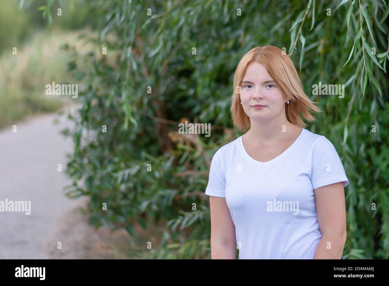 Portrait d'une jeune femme blonde heureuse en vêtements blancs. Promenade dans le parc en été, arrière-plan flou. Banque D'Images
