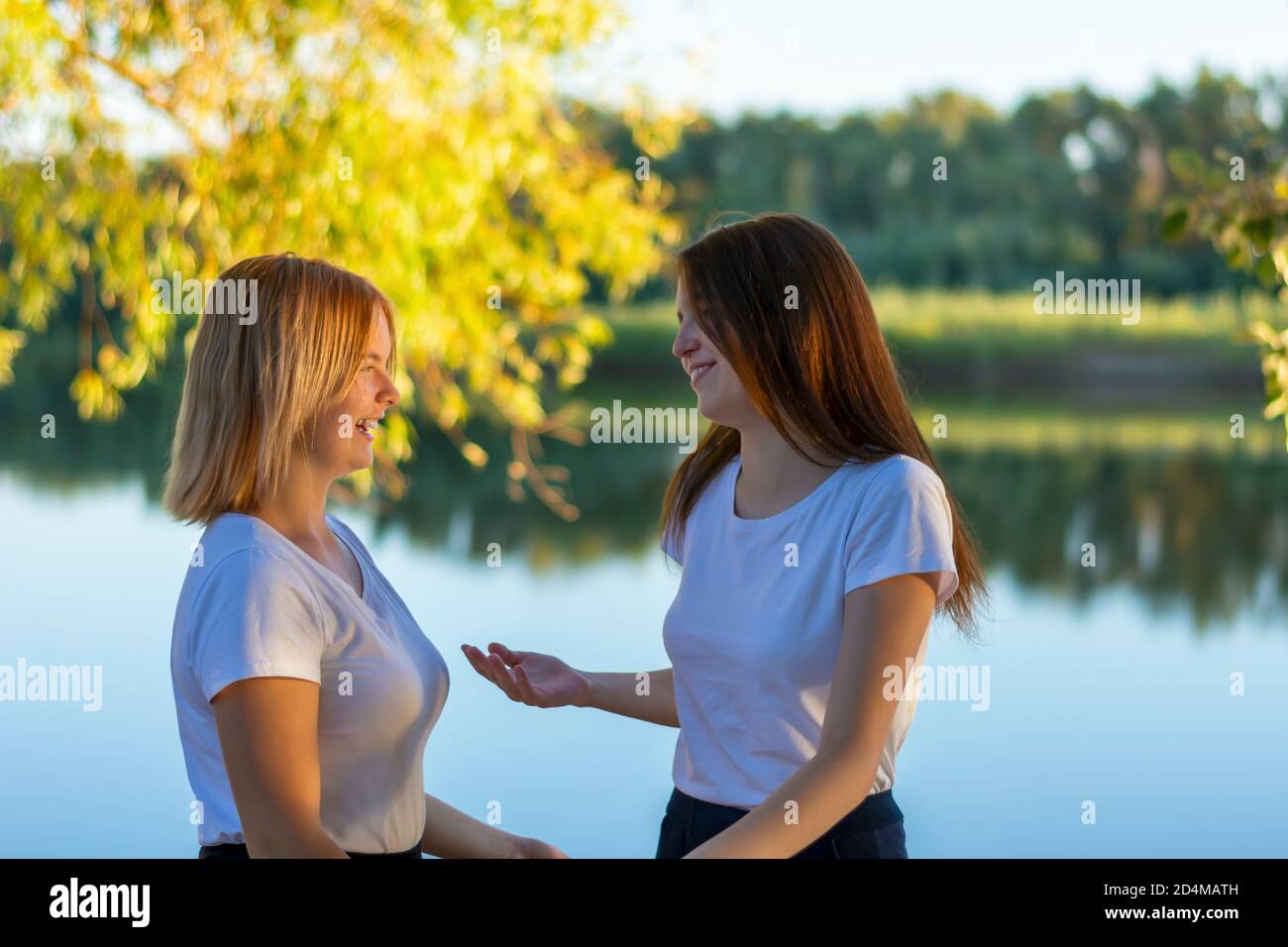 Deux jeunes femmes heureuses parlent dans le parc au bord de la rivière en automne. Amis se rencontrent, marchent, heureux ensemble. Mise au point sélective, arrière-plan flou. Banque D'Images