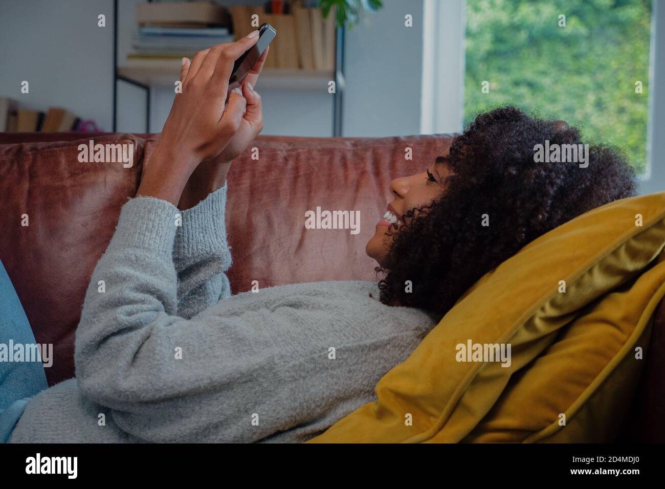 Bonne femme de course mixte recevant du texte passionnant sur smartphone tout en se reposant confortablement sur un canapé dans un salon décontracté. Banque D'Images