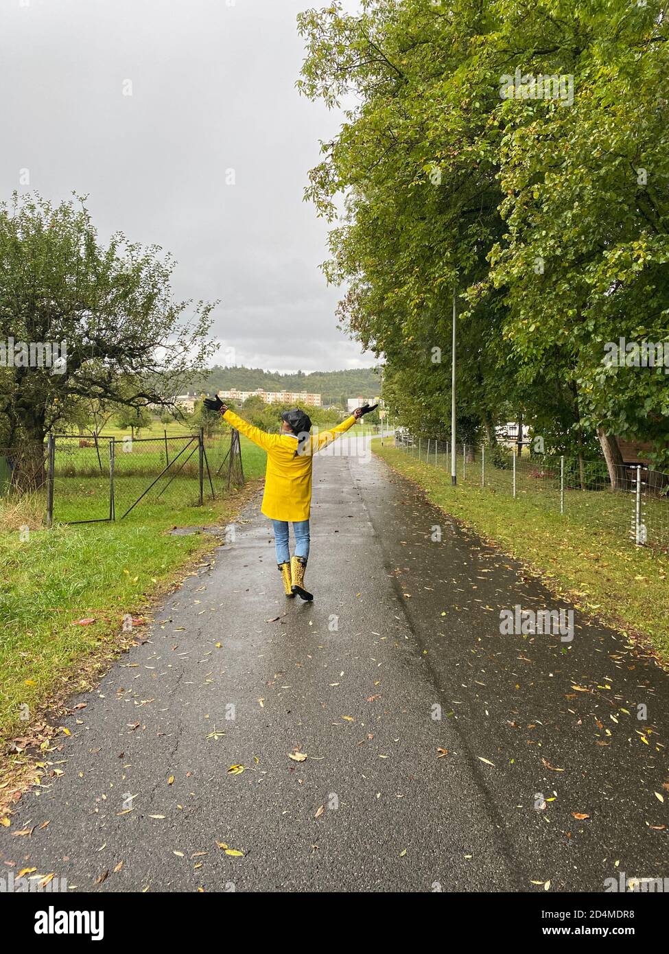 Bonne femme en imperméable jaune et bottes de pluie avec motif jaguar marchant le jour de la pluie. Vue arrière de la personne. Banque D'Images