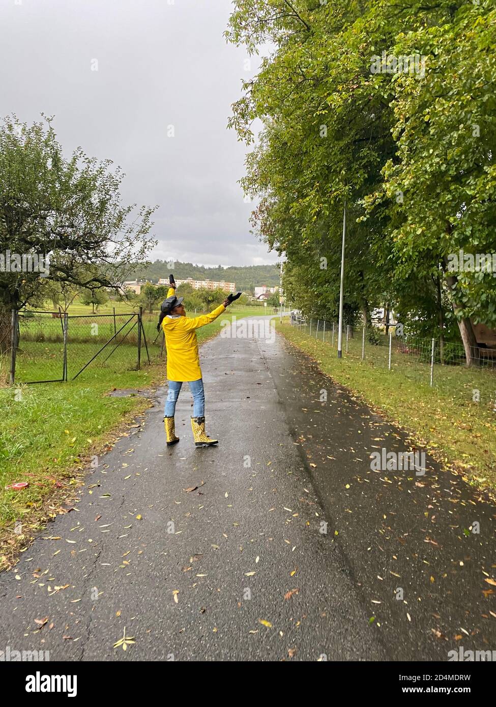 Bonne femme en imperméable jaune et bottes de pluie avec motif jaguar marchant le jour de la pluie. Vue arrière de la personne. Banque D'Images