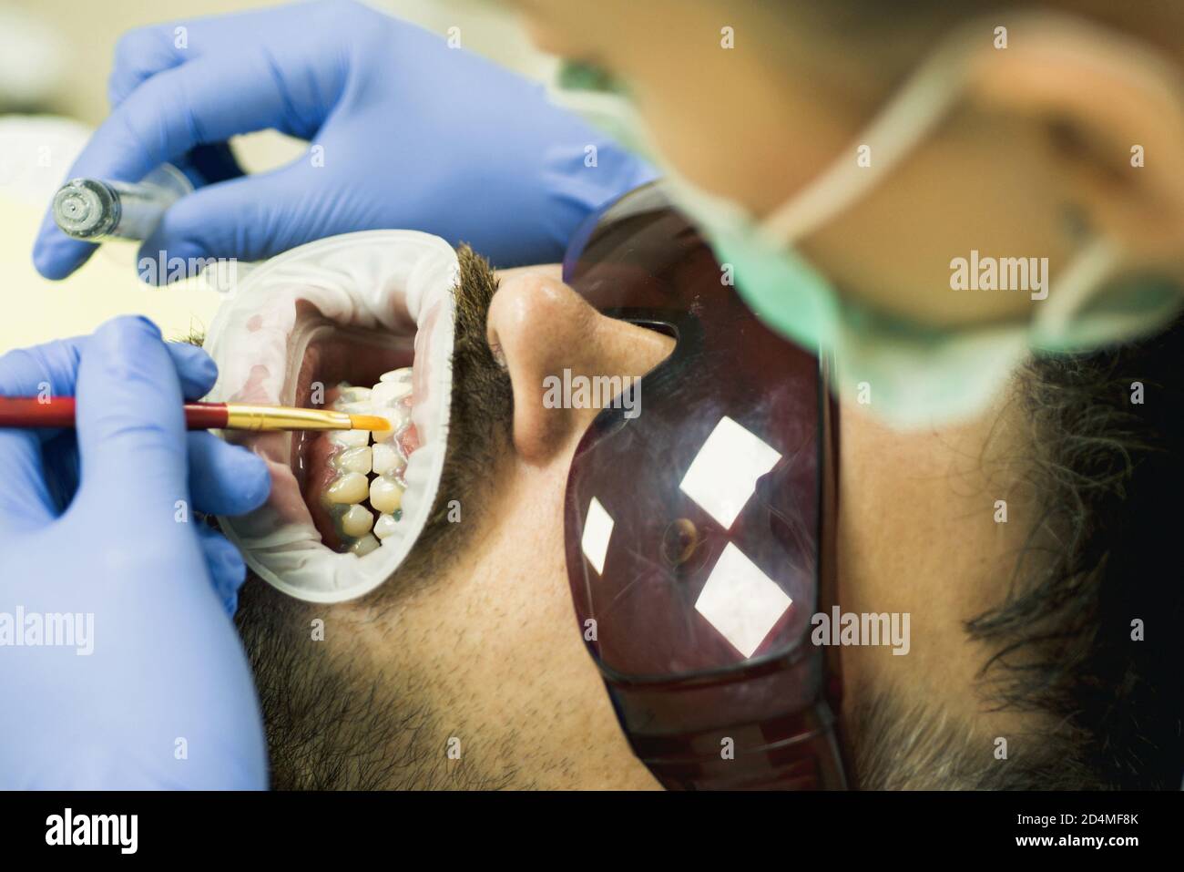 Un joli jeune homme souriant qui regarde l'appareil photo. Dentiste femme vérifiant les dents du patient avec miroir dans la clinique dentaire moderne. Examiner le jeune homme par le dentiste sur Banque D'Images