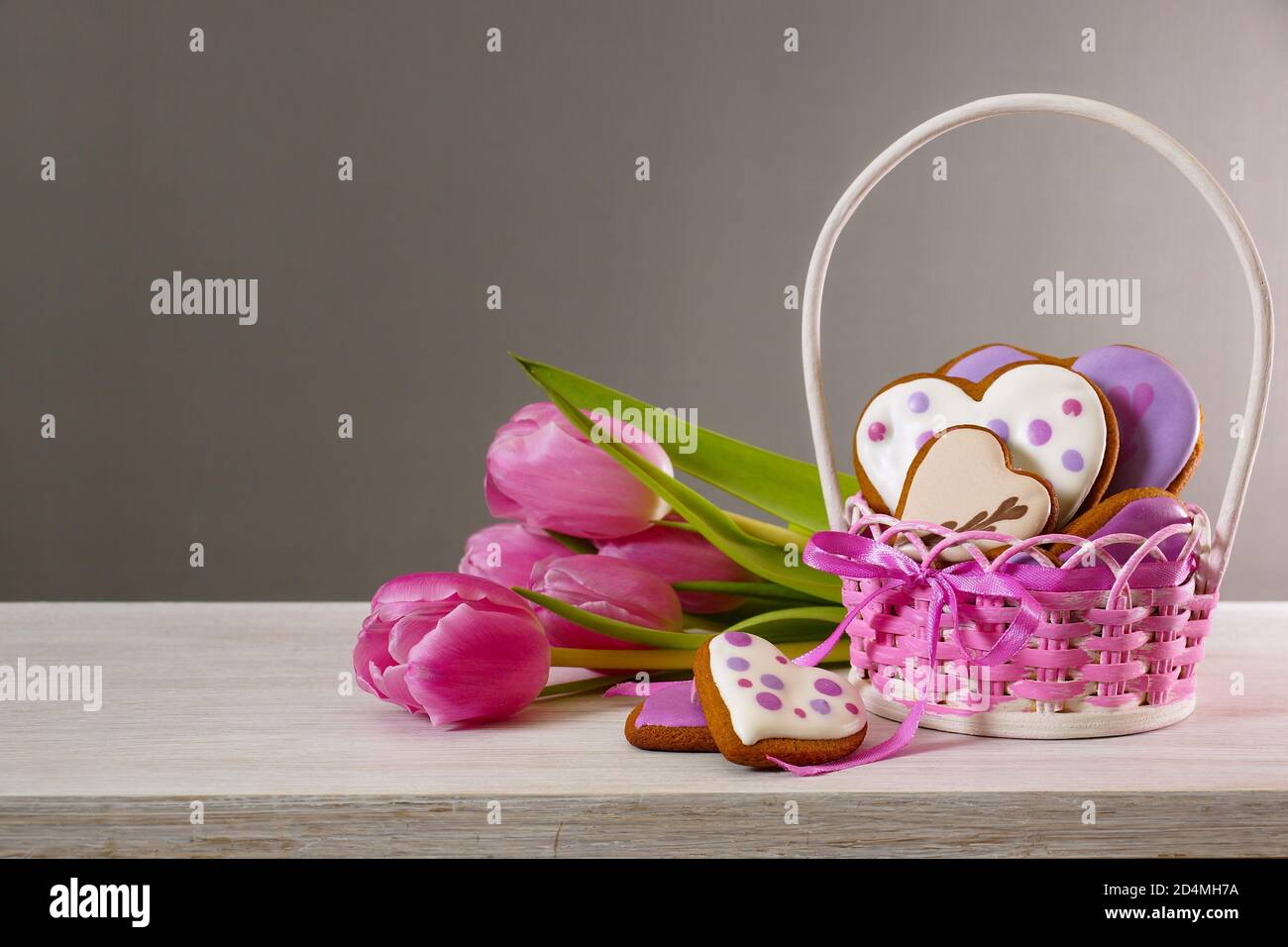 Biscuits et tulipes au pain d'épice. Pain d'épice en forme de coeur dans un panier en osier et un bouquet de tulipes. Arrière-plan gris Banque D'Images