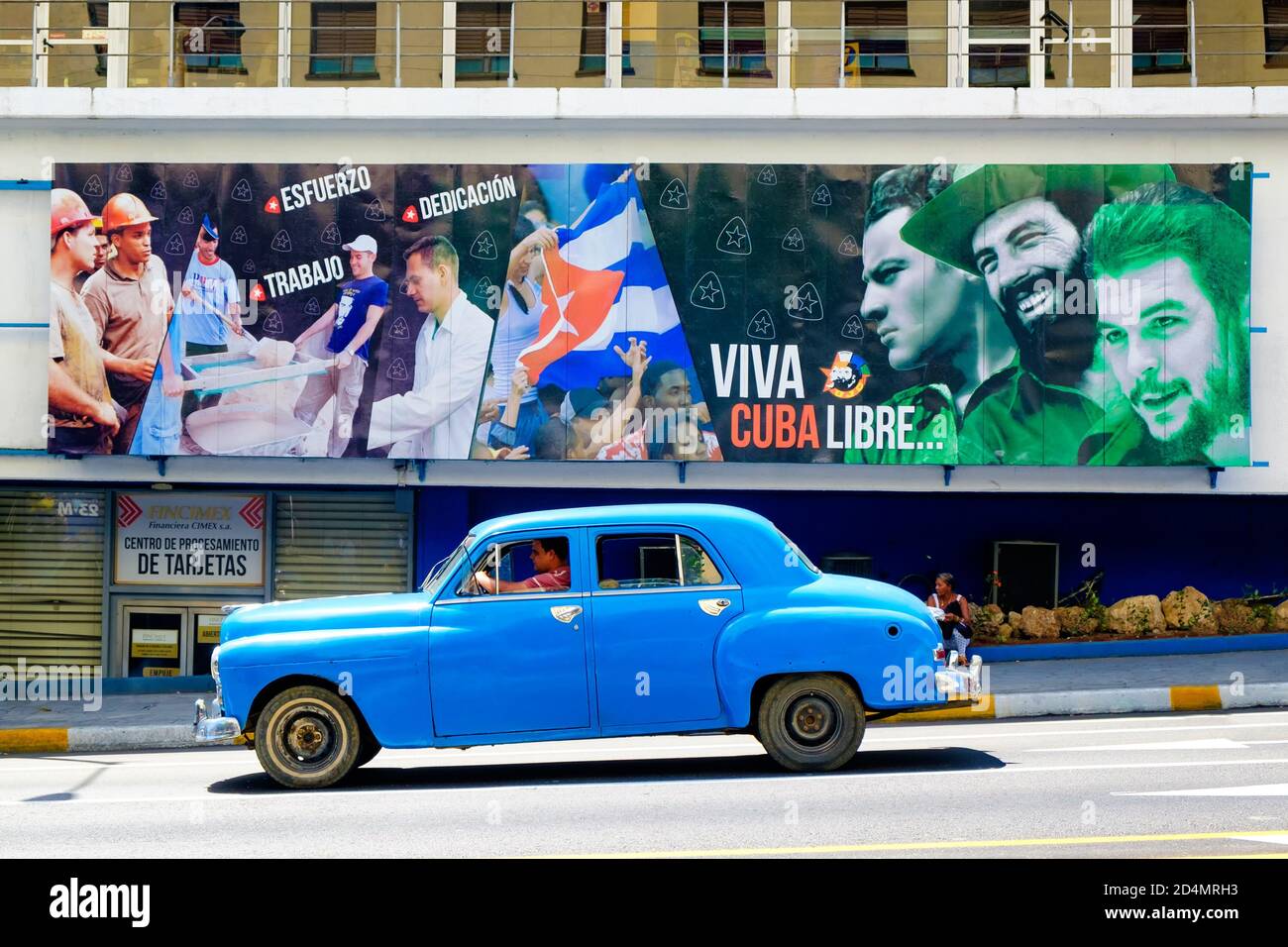 Vieille voiture classique à côté d'un panneau d'affichage avec des slogans révolutionnaires À la Havane Banque D'Images