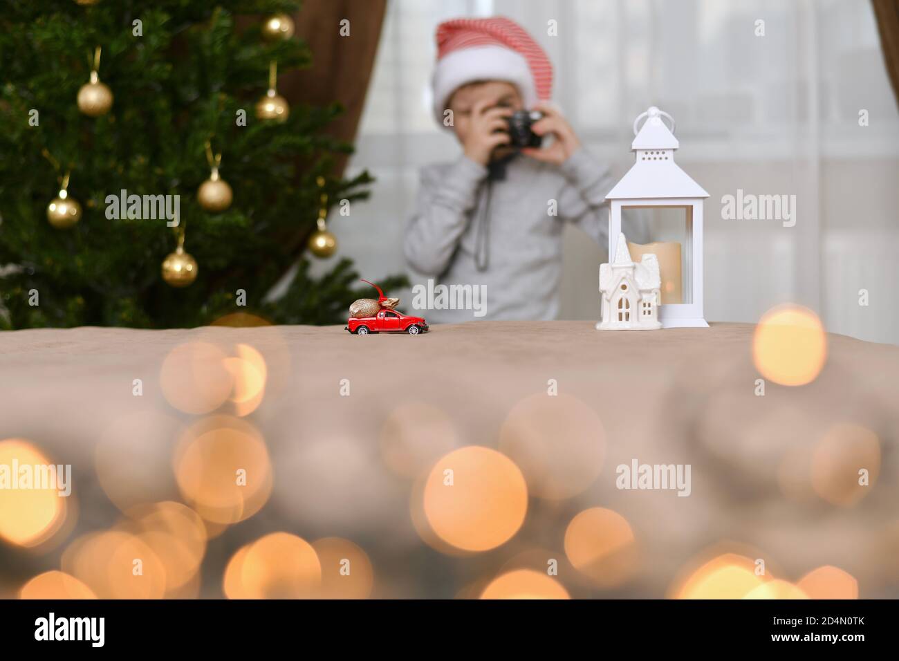 Une voiture avec un sac de cadeaux de Noël va à la maison blanche de la lanterne. Un enfant dans une casquette rayée, avec l'appareil photo. Banque D'Images