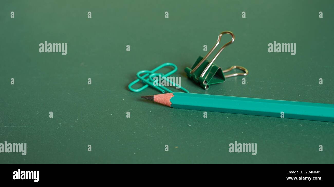 Un simple crayon et des trombones se trouvent sur un simple fond vert. Gros plan, macro Banque D'Images