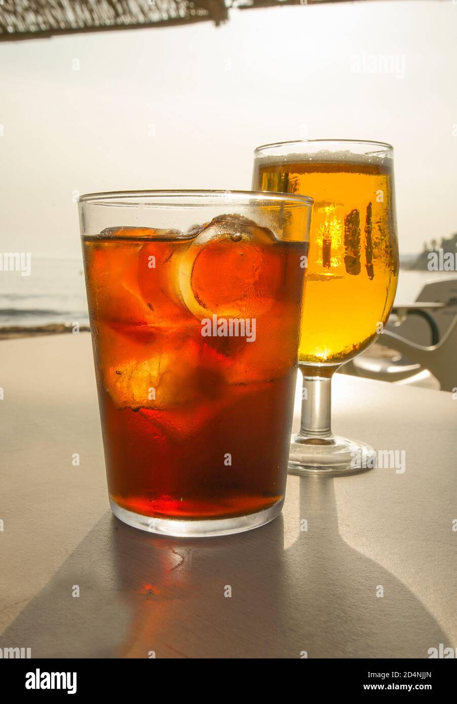 Un verre de bière et un Coca-Cola sont servis dans un restaurant de plage, avec la mer méditerranée derrière. Banque D'Images