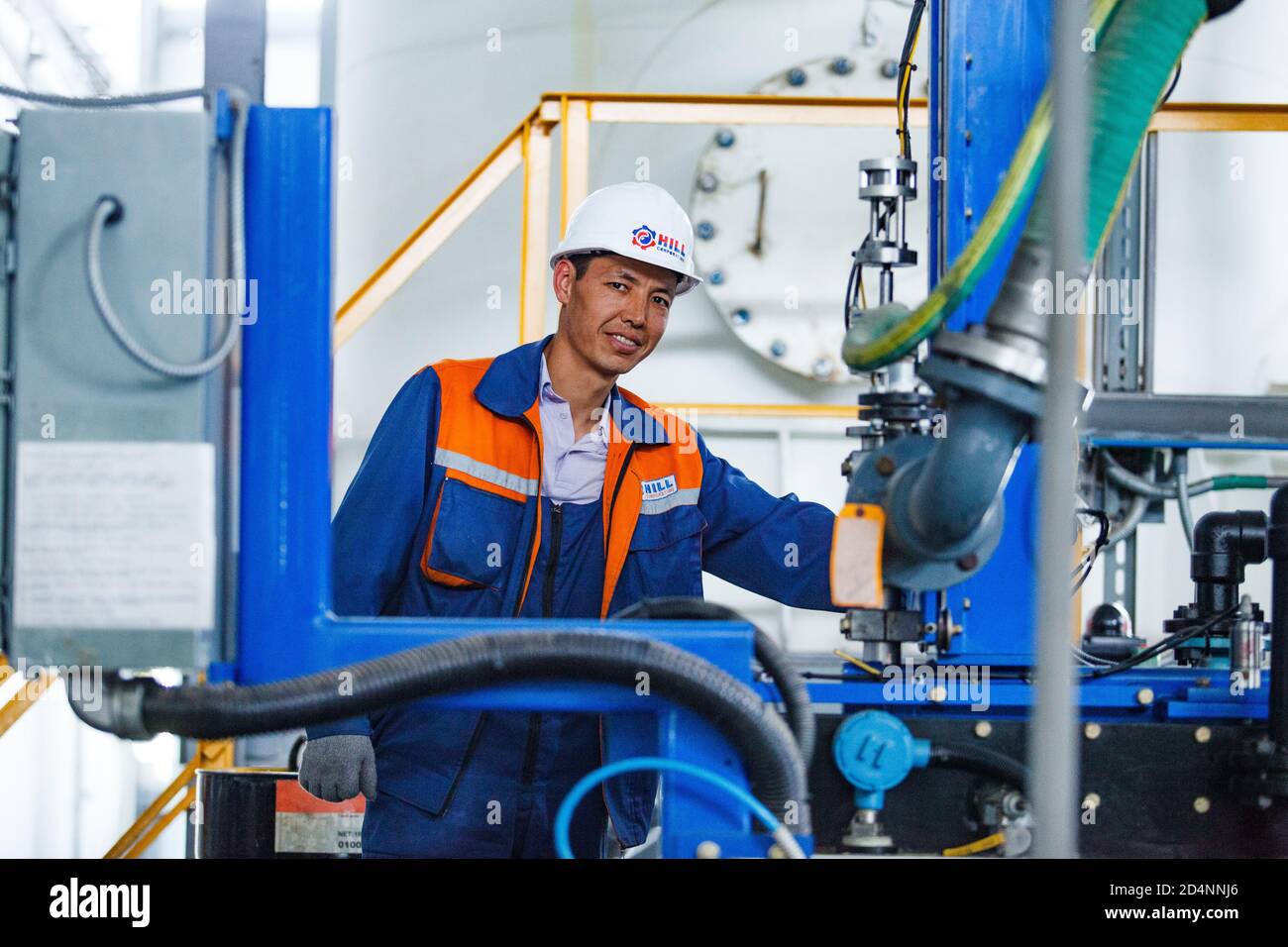 Shymkent, Kazakhstan-avril 26 2012 : usine de production moderne d'huile moteur. Souriant, jeune ouvrier asiatique, tuyaux et équipement. Arrière-plan flou. Banque D'Images