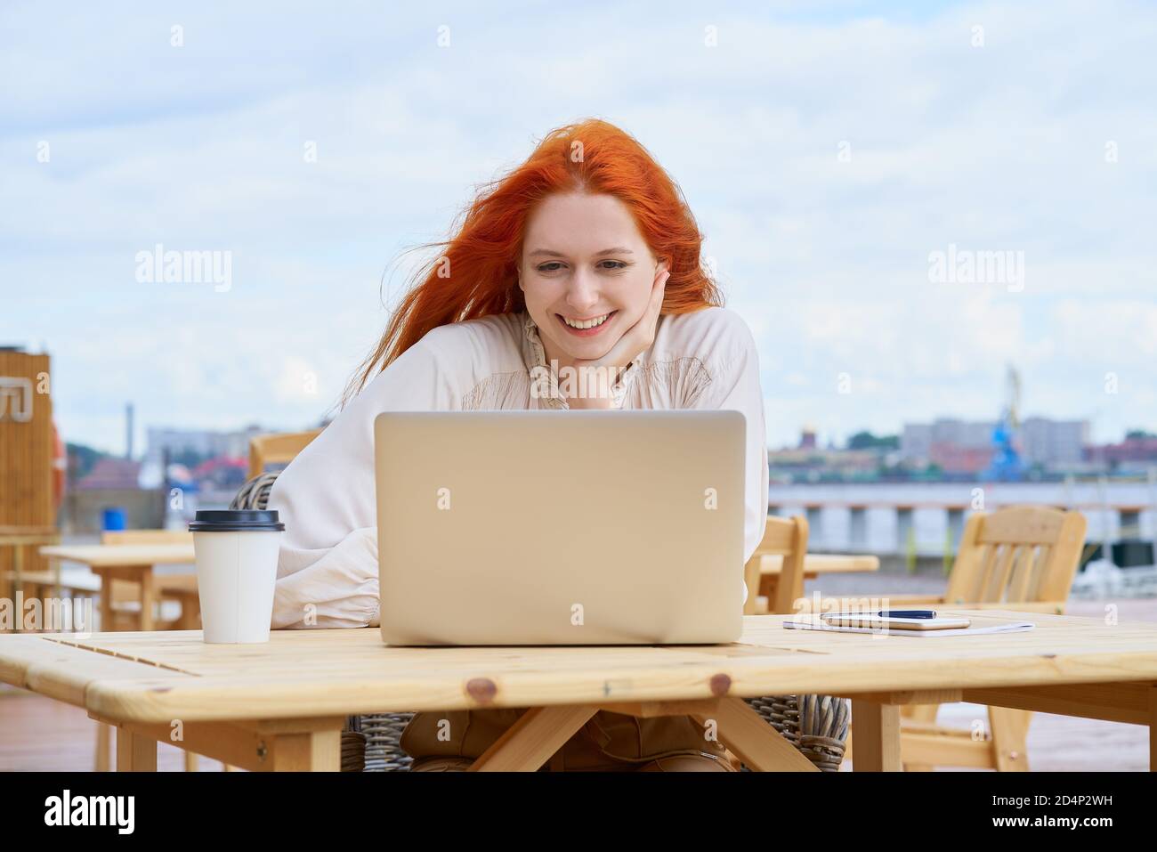 Femme indépendante assise dans un café dans la rue et travaillant à distance sur un ordinateur portable. Cours d'écoute pour les étudiantes Banque D'Images