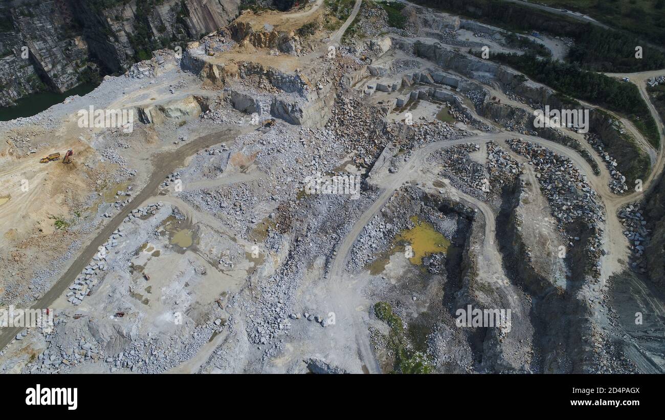 Vue aérienne de la carrière minière en plein ciel avec de nombreuses machines en service, des pelles hydrauliques et des foreuses. Vue panoramique sur la fosse en pierre. Banque D'Images