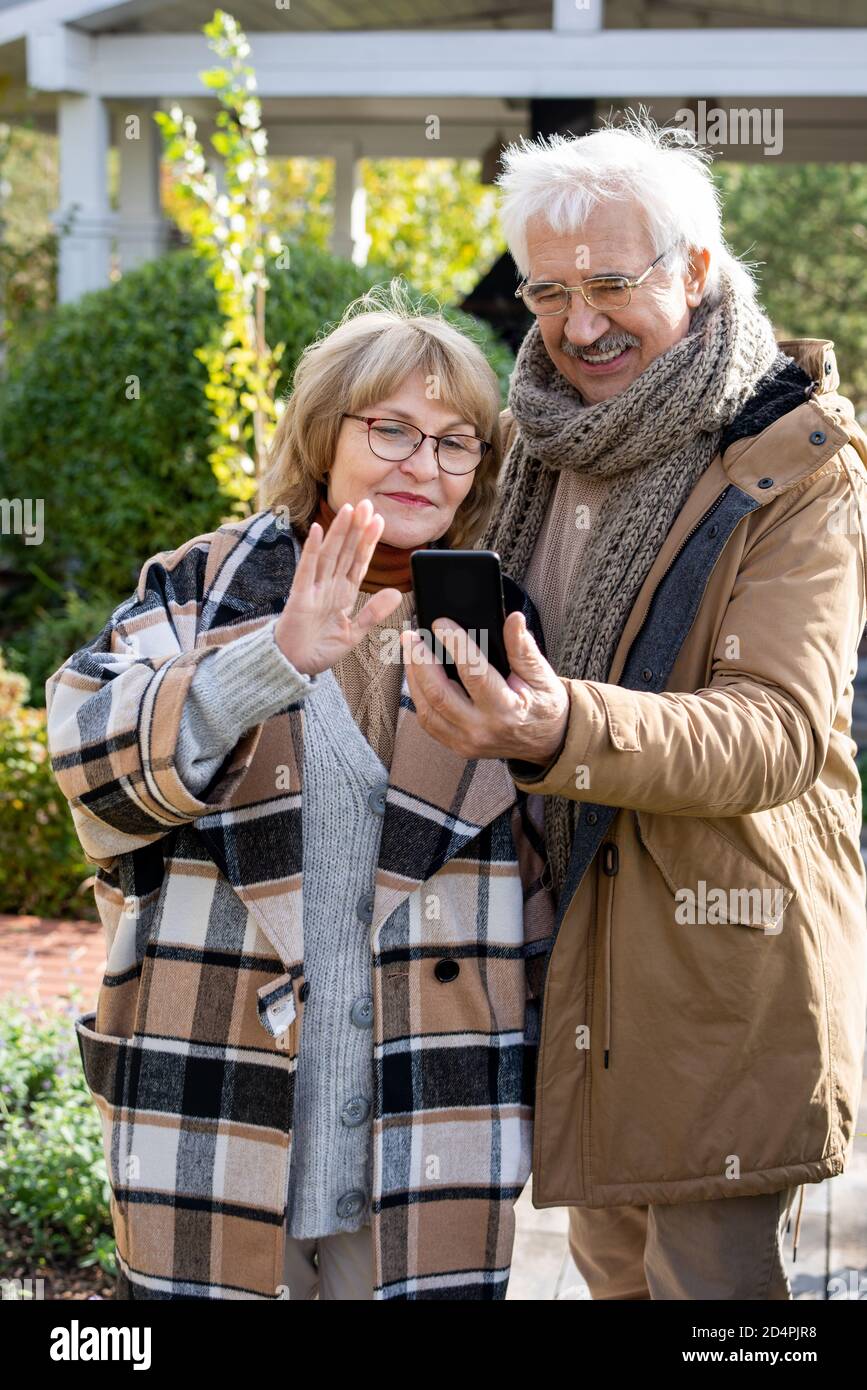 Heureux retraités conjoints dans chaud vêtements décontractés regardant leur famille dans un smartphone Banque D'Images